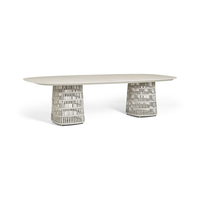 Minimalist oval dining table with a white top and patterned metal base on a plain background.